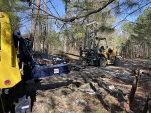 Yellow forklift sits on a dirt path surrounded by trees, with equipment and tools nearby.
