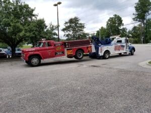 Red vintage fire truck being towed by a blue tow truck with an American flag design.