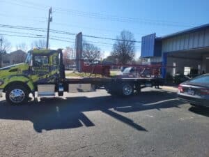 Tow truck with a bright yellow and blue design carries a large metal structure in a parking lot.