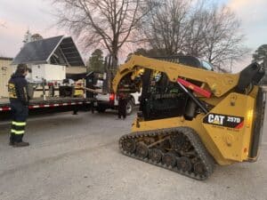 Excavator prepares to load solar equipment while workers oversee the process at a job site.