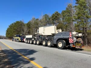 Oversized tow truck on a roadside with pine trees and a clear blue sky in the background.